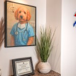Framed portrait of dog in scrubs next to plant and certificate